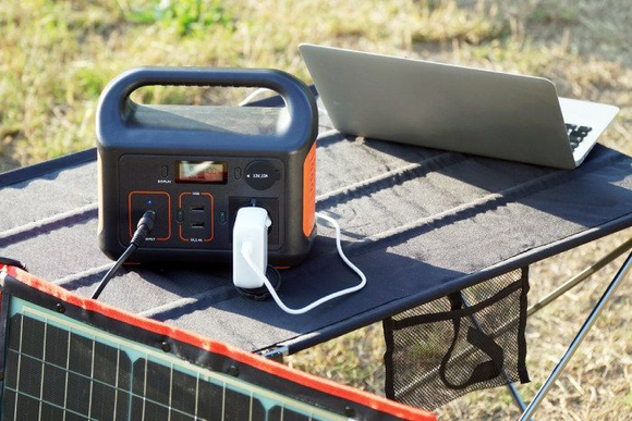 Eine Powerstation wird von einem Solarmodul geladen und versorgt einen Laptop.